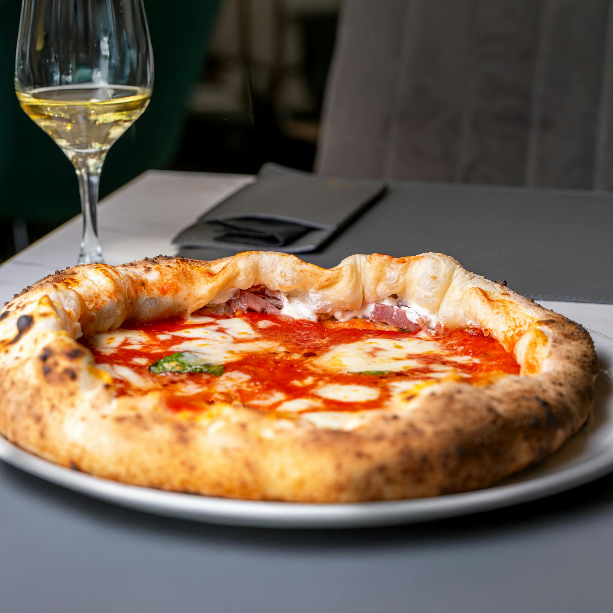 Mouthwatering Neapolitan pizza paired with a glass of white wine, perfect dining experience.